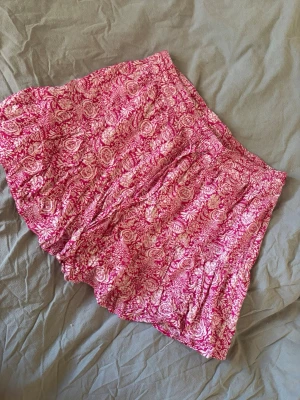 Rosa blommiga kjol med shorts  -  rosa kjol med vitt blommigt mönster och bekväm resår i midjan. Lätt och luftig med inbyggda shorts , perfekta för varma dagar. Passar dig som gillar färg och mönster!