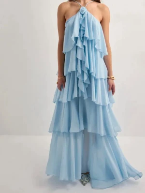 Ljusblå volangklänning med halterneck - Superfin långklänning i ljusblått med flera lager volanger och halterneck med rosettdetalj framtill. Klänningen är ärmlös och har en flowy, loose passform som ger en romantisk vibe. Perfekt för sommarens speciella tillfällen.