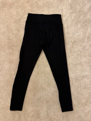 Svarta träningstights från Nike  - Säljer ett par svarta träningstights från Nike med hög midja och tight passform. Tillverkade i stretchigt material som sitter skönt på kroppen. Diskret Nike-logga på ena benet. Perfekta för träning eller chill dagar.