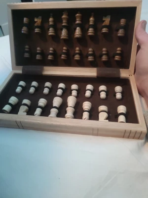 Schackspel i trä - Säljer ett schackspel i trä med vikbar bräda som även fungerar som förvaringslåda för pjäserna. Schackpjäserna är i två färger, ljusa och mörka, och brädan har klassiskt rutmönster i brunt och beige. Perfekt för schackälskare som vill ha ett stilrent set. Alla pjäser finns, finns flera små repor i bordet. Ger ett fint helhetsintryck.