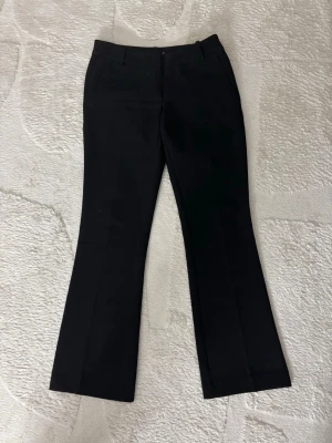 Svarta utsvängda kostymbyxor  - Snygga svarta kostymbyxor med utsvängda ben och klassisk passform. Byxorna har hällor för skärp och diskreta fickor fram. Perfekta för en stilren look och passar till många olika outfits.