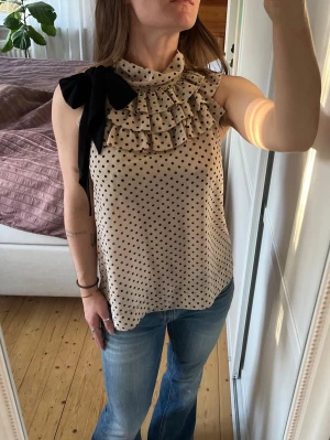 Prickig blus med volanger och rosett - Prickig topp med volanger och rosett. Rosetten är avtagbar.