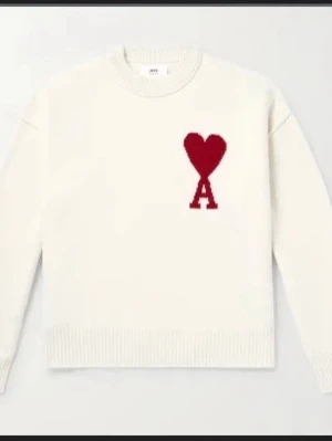 Stickad tröja från Ami Paris med hjärtdetalj - Säljer en stickad tröja från Ami Paris i två färger: vit och svart. Båda har en röd hjärtdetalj med bokstaven A på bröstet. Tröjan har rund hals, ribbade muddar och är gjord i mjukt material. Perfekt för dig som gillar stilrena plagg med en twist.