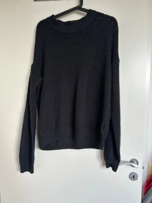 Svart stickad tröja från 157 - En svart stickad tröja från 157 med rund halsringning och ribbade muddar vid ärmslut och nederkant. Tröjan har en enkel, rak passform och är tillverkad i ett grovstickat material som ger en avslappnad look.