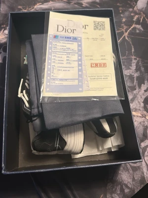 Svarta D1or sneakers med vita detaljer - Säljer ett par svarta D1or sneakers med vita och grå detaljer. Skorna har en chunky sula, vita skosnören och tydlig D1or-logga på sidan. Medföljer originalkartong, dustbag och kvitto. Perfekta för dig som gillar exklusiva sneakers och streetwear.