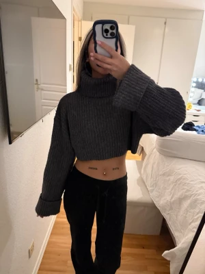 Grå cropped polotröja Gina Tricot - Mörkgrå ribbstickad cropped polotröja från Gina Tricot. Tröjan har oversized ärmar med breda muddar och hög polokrage. Perfekt för en trendig och avslappnad look. Materialet är mjukt och stretchigt för extra komfort. Passa mig som bruka ha xs-S. 