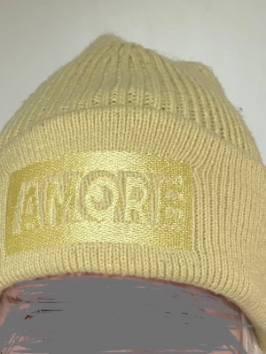 Gul mössa Onesize - Jättefin gul färg. Mössa med texten "AMORE" broderad framtill. Gina tricot. Onesize. Mössan har en uppvikt kant. Använd ett fåtal ggr, är i bra skick, inga defekter. Akryl.