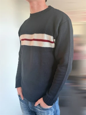 Mörkblå stickad tröja med ränder - Snygg mörkblå stickad tröja med vita och röda horisontella ränder över bröstet. Tröjan har rund halsringning, långa ärmar och ribbstickade muddar vid ärmslut och nederkant. Perfekt för dig som gillar klassisk stil med en twist.