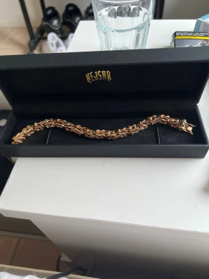 Guldigt kedjearmband från Kejsar 8mm - Snyggt armband från Kejsar med flätad kedjedesign i guldton. Armbandet har en robust och elegant look med glänsande finish och är tillverkat i metall. Perfekt för dig som vill ha ett statement piece till din outfit.