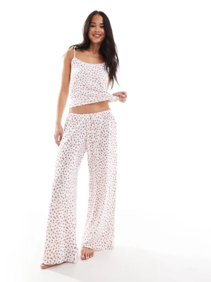 Vit pyjamas med röda blommor - Söt pyjamas i två delar med linne och vida byxor. Vit botten med små röda blommor över hela setet. Linnet har tunna axelband och spetsdetalj vid halsen. Mjukt och lätt material, perfekt för mysiga kvällar hemma.