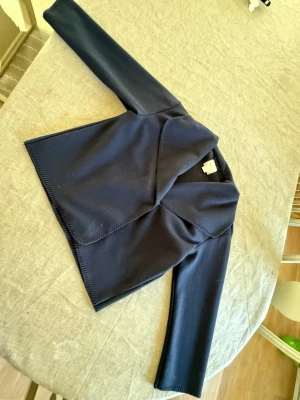 Mörkblå kofta från Gina Tricot - Snygg mörkblå kofta från Gina Tricot med lång ärm och öppen front. Koftan har en modern, lite asymmetrisk skärning och är tillverkad i ett mjukt och stretchigt material. Perfekt att slänga på sig över en t-shirt eller topp.