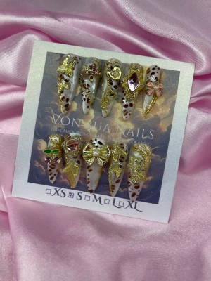 OjouDrip (S);Long Stiletto - Unika handgjorda press-on naglar i leopardmönster med långa spetsiga stilettoform. Dekorerade med 3D-gulddekorationer som rosetter, fjärilar, hjärtan och stenar i rosa och grönt. Perfekt för dig som vill sticka ut med glam och detaljer. Handgjorda och exklusiva.S: 15 mm, 11,5 mm, 12 mm, 11 mm, 9 mm 