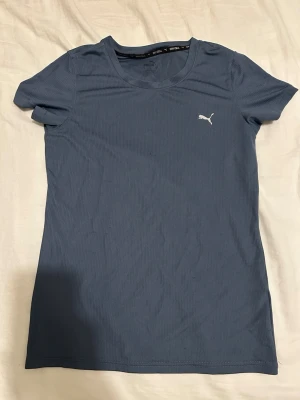 Blå träningströja från  Puma - Snygg blå t-shirt från Puma med diskret ribbad struktur och klassisk passform. T-shirten har korta ärmar och en liten vit Puma-logga på bröstet. Perfekt till tränings tillfällen. För liten för mig som är M då den är storlek S