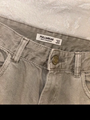 Beige cargobyxor från Pull&Bear - Säljer ett par beige cargobyxor från Pull&Bear med raka ben och stora fickor på sidorna. Byxorna är tillverkade i bomull och har klassisk knappstängning samt hällor för bälte. Perfekt för dig som gillar en avslappnad och trendig stil.