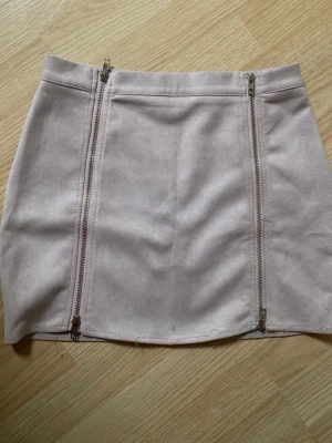 Ljusbeige/rosa mockakjol med dragkedjor - Supersnygg ljusbeige/rosa kjol i mockaimitation från Boohoo (tror jag). Kjolen har en tight passform och coola detaljer med två vertikala dragkedjor framtill. Perfekt för att lyfta vilken outfit som helst! Nedersta sömmarna har gått upp lite men det är inget som syns så mycket.