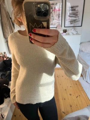 Krämvit stickad tröja Vero Moda - Mysig krämvit stickad tröja från Vero Moda med rund halsringning och ribbade muddar. Tröjan har en enkel och stilren design som passar perfekt till jeans eller kjol. Materialet är mjukt och behagligt mot huden.