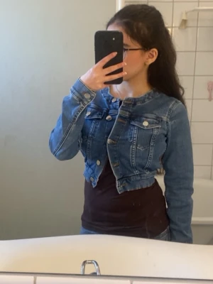 NAKD JEANSJACKA - Snygg kort jeansjacka i klassisk blå denim med silverfärgade knappar och två bröstfickor med lock. Jackan har en figurnära passform och markerade sömmar som ger en cool look. Perfekt att slänga över en t-shirt eller klänning. Super söt och skön