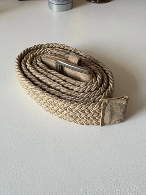 Beige flätat bälte i bomull - Säljer nu detta snygga beigea flätade bälte från Selected med silverfärgat spänne och detaljer i mocka. Bältet är gjort i bomull och har en stilren, avslappnad look som passar till många outfits. Bältet är stretchbart så går lite att anpassa längden men den outstretchbara längden är 106 cm. Inga tecken på slitage. Öppen för frågor! 🙂😁