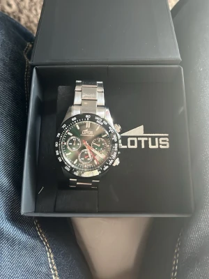 Silverfärgad klocka från Lotus - Snygg klocka från Lotus i silverfärgat rostfritt stål med länkarmband och svart urtavla. Klockan har tydliga siffror och markeringar på ringen samt klassisk sportig design. Perfekt accessoar för dig som gillar stilrena detaljer. Original pris 2400 online àå repor som knappast syns om man inte kollar noga 