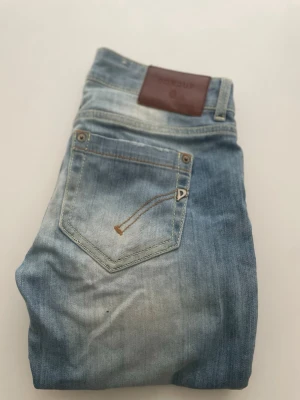 Ljusblå jeans från Dondup - Snygga ljusblå jeans från Dondup med klassisk femficksdesign och läderpatch bak i midjan. Jeansen har en tvättad look med slitningar och kontrastsömmar. Perfekta för en avslappnad och trendig stil.