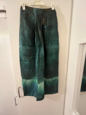 Grön långkjol  - Snygg långkjol  i skimrande grönt siden med unikt färgskiftande mönster. Kjolen har rak passform och subtila nyanser av mörkgrönt och ljusare grönt nertill. Kjolen är HELT ny köpt utomlands och den passar både storlek 34 och 36!