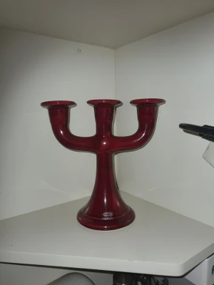 Vinröd ljusstake från Guldkroken - Säljer en vinröd ljusstake i glas från Guldkroken Hjo, Sweden. Ljusstaken har plats för tre ljus och har en modern, rundad form som sticker ut i inredningen. Perfekt som dekoration på bordet eller i fönstret.