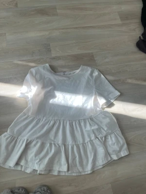 Vit volangtopp med kort ärm - Säljer en söt vit topp med volanger och korta ärmar. Den har en rund halsringning och är tillverkad i ett mjukt bomullsmaterial. Perfekt för dig som gillar en luftig och avslappnad stil.