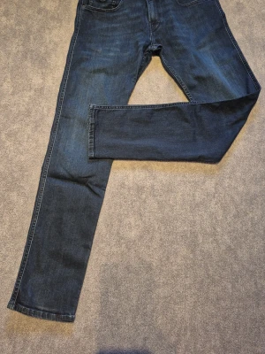 Replay anbass slim fit jeans - Snygga mörkblå jeans i en slim fit modell med normalhög midja och avsmalnande ben. Femficksmodell med dragkedja i gylfen. Jeansen är tillverkade i denim med lite stretch för extra komfort. Perfekt för dig som gillar en enkel och stilren look.