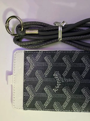  korthållare med snodd - Snygg korthållare från med i grått och vitt med klassiskt mönster. Har ett fönster för ID-kort på ena sidan och medföljande snodd med metallring, perfekt att hänga runt halsen. Tillverkad i canvas och läder. Perfekt accessoar för att hålla koll på dina kort.