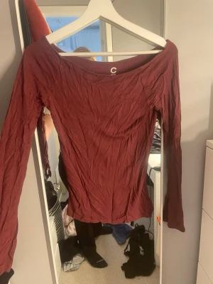 Mörkröd långärmad topp från C - Snygg mörkröd långärmad topp från C med bred, något båtformad halsringning. Tillverkad i mjuk bomull som känns skön mot huden. Perfekt att styla med jeans eller kjol för en trendig look.