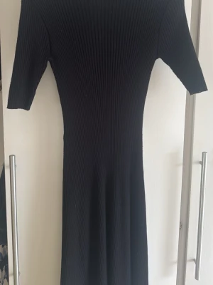 Svart ribbad klänning från Lindex - Säljer en svart ribbad klänning från Lindex i storlek S. Klänningen har korta ärmar, rund halsringning och är gjord i ett stretchigt material som sitter snyggt på kroppen. Perfekt för dig som gillar enkel men stilren design.