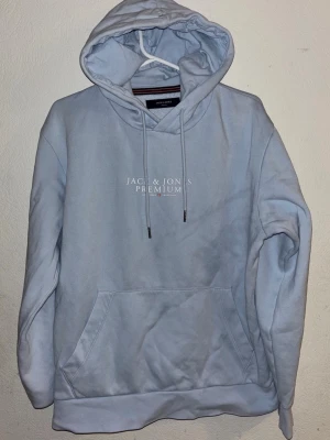 Ljusblå hoodie från Jack & Jones - Ljusblå hoodie från Jack & Jones Premium med vit logga på bröstet. Klassisk modell med stor känguruficka framtill, justerbar dragsko i huvan och mjukt material. Perfekt för en avslappnad och stilren look. Använder den inte längre och den ligger där, kan diskutera pris vid snabbäfare. Riktig bra kvalitet. För mer information hör av er