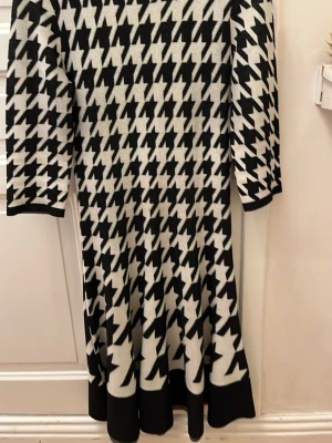 Svartvit mönstrad klänning Derhy K - Säljer en svartvit klänning från Derhy K  med hundtands mönster. Klänningen har trekvartsärm, rund halsringning och är i mjukt stickat material. Perfekt för dig som gillar grafiska prints och vill sticka ut lite extra.