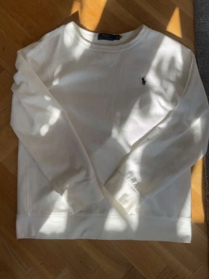 Vit sweatshirt från Polo Ralph Lauren - Klassisk vit sweatshirt från Polo Ralph Lauren med rund halsringning och broderad logga på bröstet. Tröjan har långa ärmar och ribbade muddar. Perfekt för en clean och stilren look.