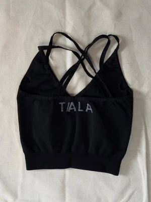 Svart sport-bh från Tiala - Snygg svart sport-bh från Tala med tunna korsade axelband och bred resår nedtill. Perfekt för träning eller yoga. Mjukt och stretchigt material som ger bra stöd och komfort.