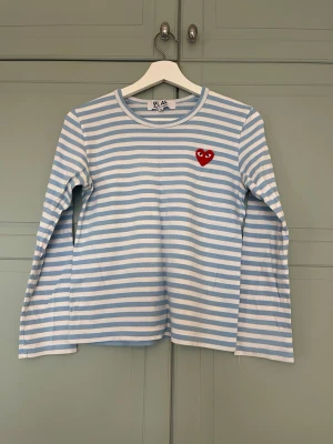 Randig långärmad tröja från Comme des Garçons - Säljer min sambos ljusblå - och vit randiga långärmade tröja från Comme des Garçons PLAY. Tillverkad i mjuk bomull. I mycket bra skick. Köpt på Farfetch & kvitto finns.