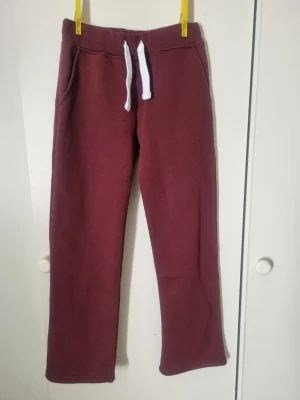 Vinröda mjukisbyxor med dragsko XS Russe Merch - Mysiga vinröda mjukisbyxor från RusseMerch med vita dragsnören och fickor på sidorna. Byxorna har rak passform och är tillverkade i ett mjukt och bekvämt material, perfekt för chill dagar hemma eller när du vill vara extra bekväm. Endast provade men lappen föll bort