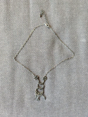 Silvrigt halsband med detaljerad hänge - Unikt silvrigt halsband med ett hänge i flera nivåer, dekorerat med små blommor och pärlliknande detaljer. Kedjan är tunn och smidig, och hänget har en bohemisk känsla med sina små utsmyckningar och former. Perfekt för dig som gillar personliga accessoarer.