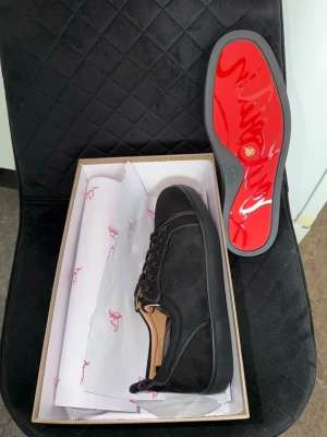 Svarta Christian Louboutin - Svarta Christian Louboutin i mocka med klassisk röd sula. Skorna har svarta skosnören, diskreta sömmar och en låg profil. Perfekta för dig som vill ha en exklusiv och stilren look med den ikoniska röda sulan.