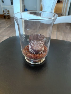Glaslykta med dekor och stenar - Säljer en glaslykta med ingraverade stjärnmönster och en innerdel i lila glas med vit dekor. Botten är fylld med små röda dekorationsstenar. Perfekt som ljuslykta för värmeljus och ger mysig stämning.