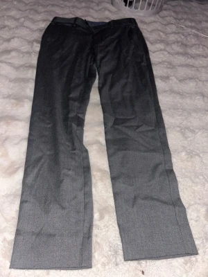 Grå kostymbyxor med klassisk passform - Snygga grå kostymbyxor med raka ben och klassisk passform. Byxorna har diskreta fickor och är tillverkade i ett slätt material som ger en stilren look. Perfekta för dig som vill ha en clean och enkel stil.