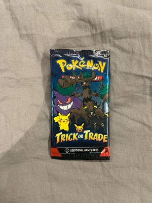 Pokémon Trick or Trade boosterpack - Säljer ett Pokémon Trick or Trade boosterpack med färgglad design och motiv av Pikachu, Gengar och andra Pokémon. Förpackningen är blå med gula och lila detaljer och innehåller samlarkort till Pokémon Trading Card Game.