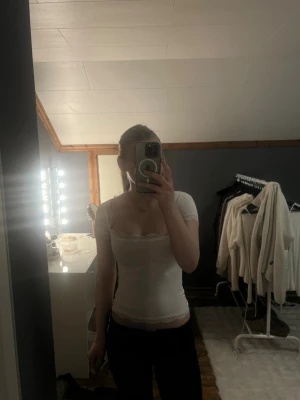 Vit topp med spets från Gina Tricot - Söt vit topp från Gina Tricot med korta ärmar och fyrkantig urringning. Toppens kanter är dekorerade med fin spets och den är figurnära i modellen. 