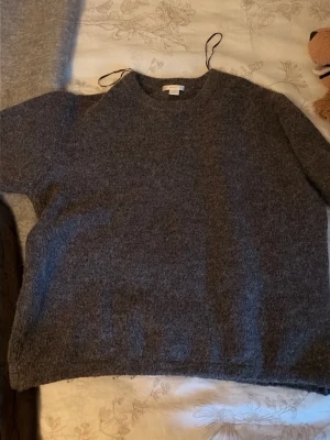 Mörkgrå stickad tröja Gina Tricot - Mysig mörkgrå stickad tröja från Gina Tricot med rund halsringning och lång ärm. Tröjan har en fluffig, mjuk yta och enkel design som passar perfekt till jeans eller kjol. Materialet känns varmt och skönt för kyligare dagar.