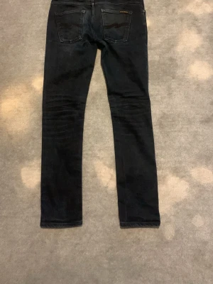 Svarta slim fit jeans från Nudie - Svarta slim fit jeans från Nudie med klassisk femficksdesign och diskreta sömmar. Jeansen har en smal passform och är tillverkade i ett stretchigt denimtyg för extra komfort. Perfekta för en stilren och avslappnad look.