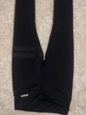 Svarta leggings från Stronger - För kvinnor Snygga svarta leggings från Stronger med två diskreta randiga detaljer på ena benet. Tillverkade i stretchigt funktionsmaterial som sitter skönt och följsamt. Perfekta för träning eller chill. Logga på benet. Använda en gång❤️