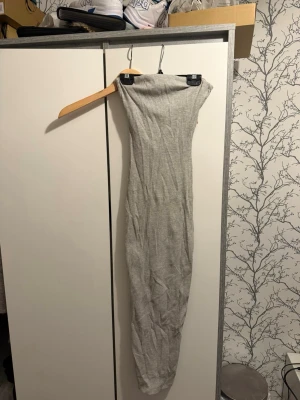 Grå ribbad långklänning - Säljer en grå ribbad långklänning med tight passform och axelbandslös design. Klänningen är enkel och stilren, perfekt för dig som gillar minimalistisk stil. Materialet är stretchigt och följsamt.