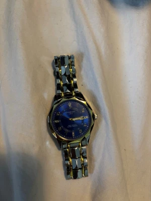 BANGON blå och guld klocka - Stilren klocka från BANBONY med blå urtavla och guldfärgade detaljer. Armbandet är i metall med både silver- och guldfärgade länkar. Klassisk rund form och tydliga siffror på urtavlan. Perfekt accessoar för dig som vill sticka ut.