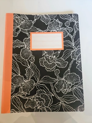 Snyggt anteckningsblock med blommönster - Anteckningsblock med svart omslag och vita blommor i linjemönster. Ryggen och etiketten på framsidan är i korallrosa. Perfekt för skolarbete, dagbok eller kreativa idéer. Pappersmaterial och stilren design.