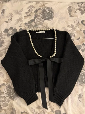 Svart kofta med pärldetalj från ZARA - Superfin svart kofta från ZARA med pärlor längs urringningen och en satinrosett framtill 🤍Använd endast en gång!